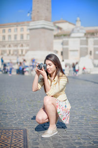 Full length of beautiful woman photographing by historic building against sky