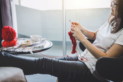 Woman knitting wool while sitting on chair at home