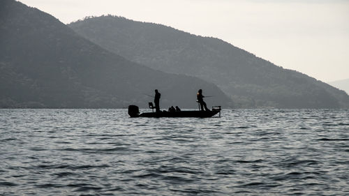 Silhouette people on boat in sea against sky