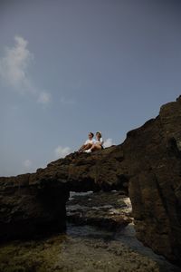 Low angle view of couple on rock against sky