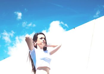 Low angle view of young woman standing against blue sky