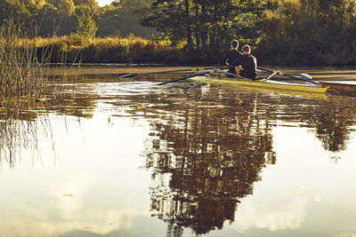 People sitting by lake against trees