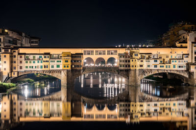 Ponte vecchio with reflection over arno river against sky at night