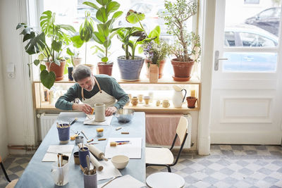 Mature man making craft product at table in pottery class