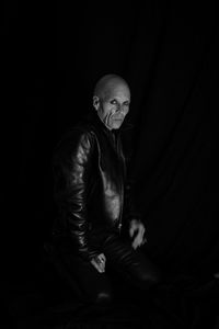 Portrait of man sitting against black background