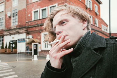 Young man smoking cigarette while looking away in city during winter