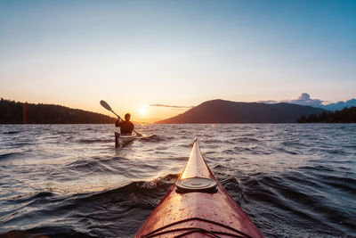 Rear view of person in sea against sky during sunset