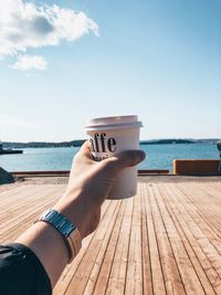 Man holding drink at sea against sky