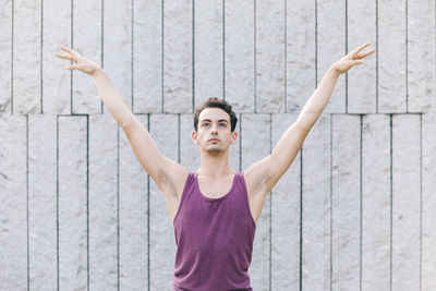 Portrait of woman with arms raised standing against wall