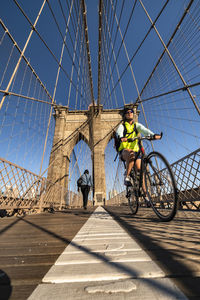 People riding bicycle on bridge against sky