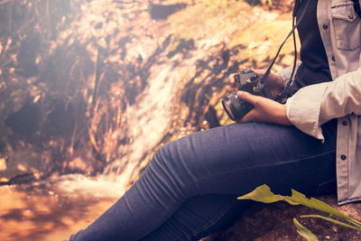 Midsection of woman holding camera while sitting on rock