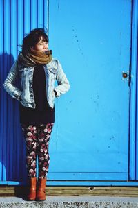 Full length of young woman standing against blue door