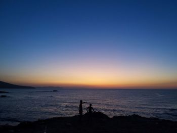 Silhouette people on beach against sky during sunset