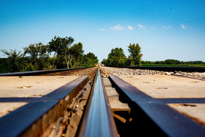 Railroad tracks by trees against blue sky