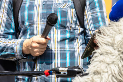 Reporter holding microphone and mobile phone during news conference, press interview or media event