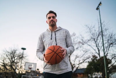 Man holding ball while standing by tree against sky