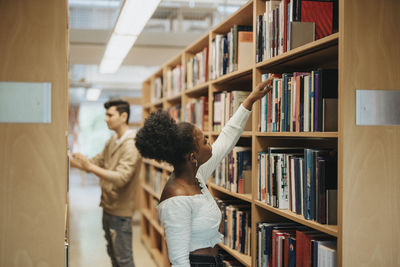 Side view of student searching books on bookshelf in library at university