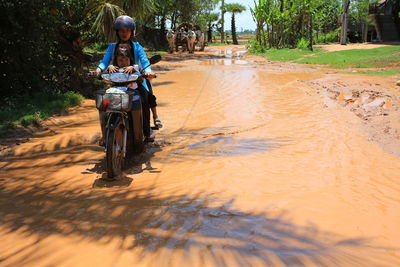 Woman with daughter riding motorcycle on muddy road