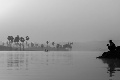 Silhouette people by lake against clear sky