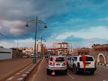 Cars on street by buildings against sky in city