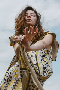 Low angle view of young woman standing against cloudy sky