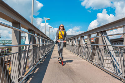 Low angle view of girl riding push scooter over footbridge