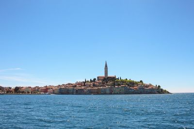 View of sea by city against clear blue sky