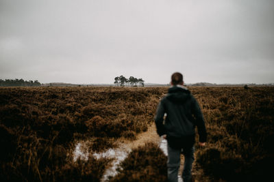 Rear view of man walking on field against sky