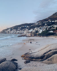 Full length of man crouching with dog on beach against townscape