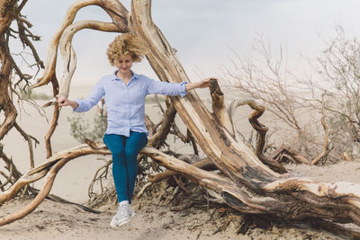 Full length of young woman sitting on bare tree