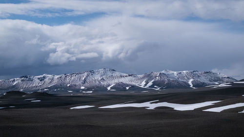 Scenic view of landscape and snowcapped mountains against cloudy sky