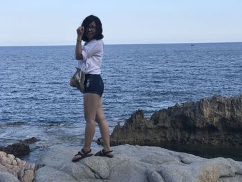 Young woman standing on rock by sea against clear sky