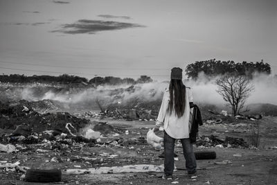 Rear view of woman standing against junkyard