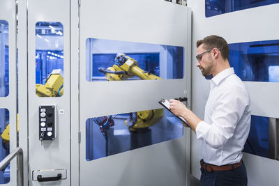 Man taking notes at robotics machine in factory shop floor