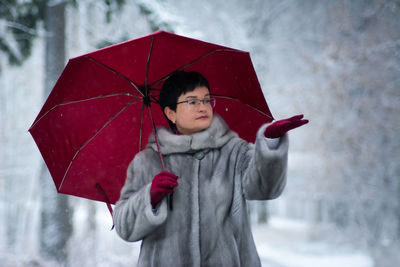 Woman in a gray fur coat with a red umbrella stands on a white, snow-covered background.