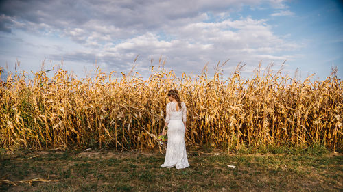 Rear view of woman in wedding dress standing against field