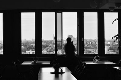 Woman sitting on table by window against sky