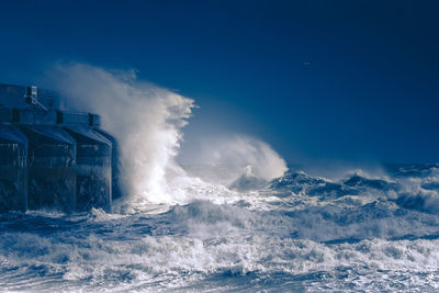 Waves breaking against sea against blue sky