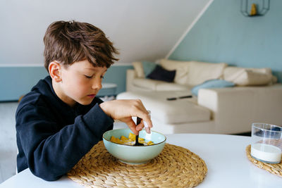 The boy sits over the plate and does not want to have a breakfast. no appetite.