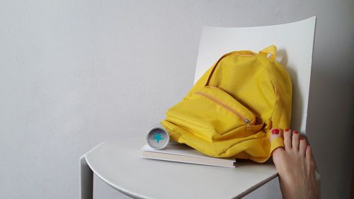 Low section of woman by backpack and book on chair against white wall 