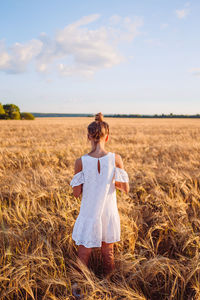 Rear view of woman standing on field against sky