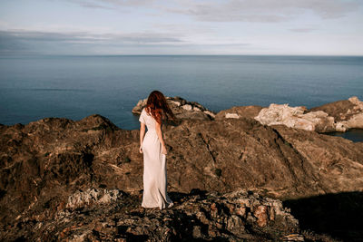 Man standing on rock by sea against sky