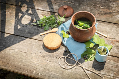 Clay jar with natural cucumbers, black currant, herbs and spices on a wooden table