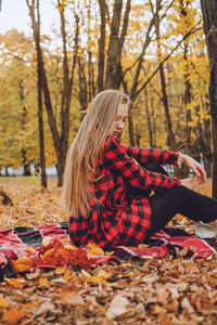 Full length of young woman sitting on tree during autumn