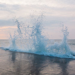 Sea waves splashing on shore against sky