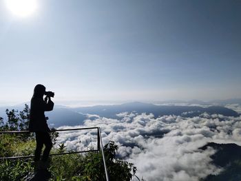 Man photographing through camera on mountain against sky