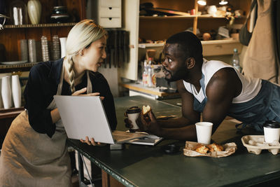 Female entrepreneur explaining male colleague over laptop in upcycling store