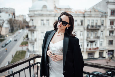 Young woman wearing sunglasses standing against railing in city