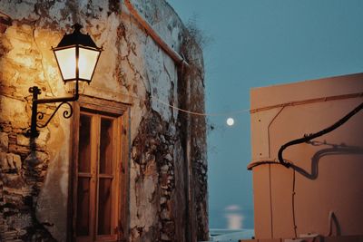 Low angle view of illuminated street light by building against sky