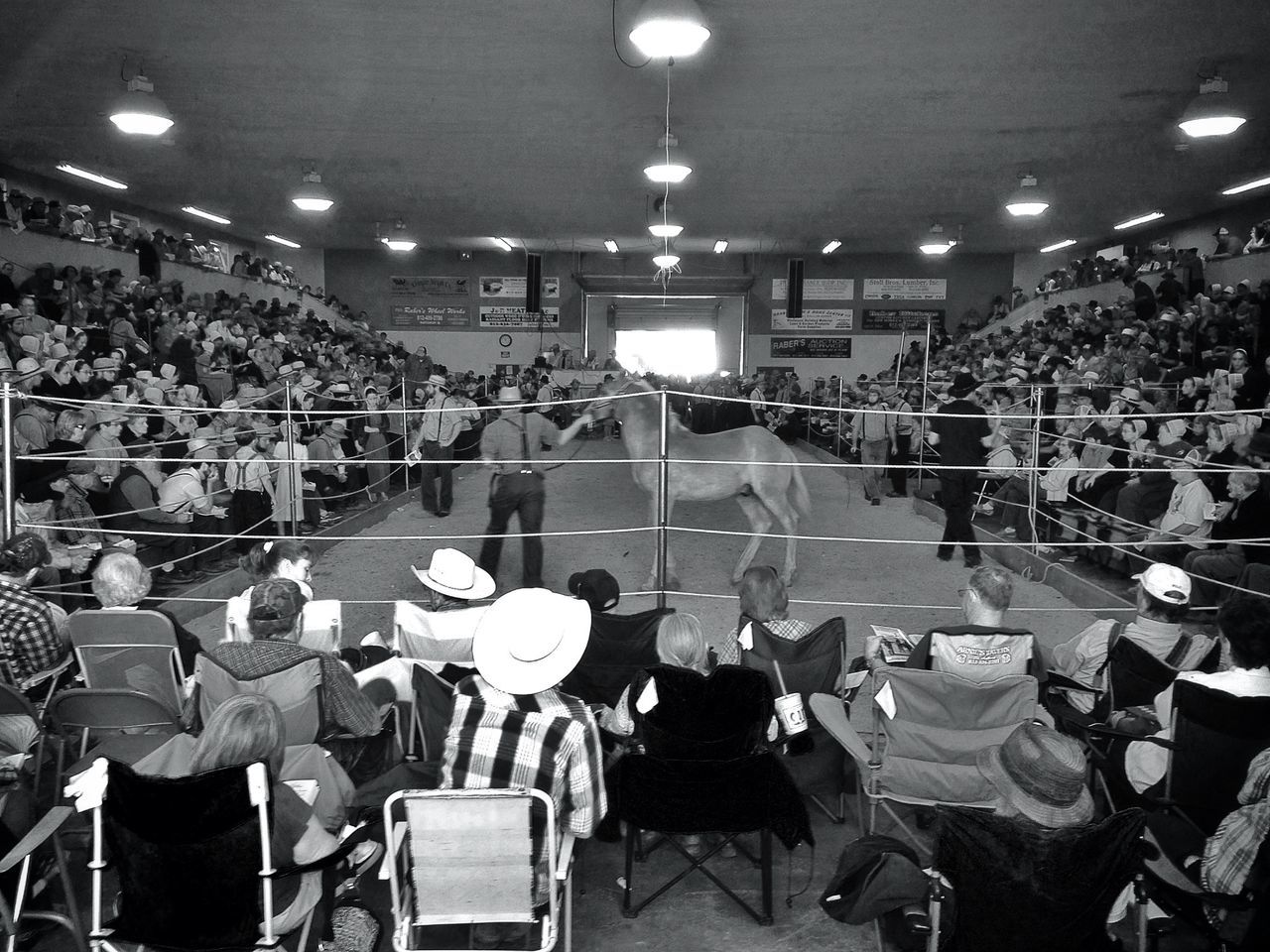 large group of people, illuminated, chair, men, restaurant, person, table, crowd, indoors, night, lighting equipment, lifestyles, leisure activity, sitting, in a row, stadium, arts culture and entertainment, abundance, arrangement